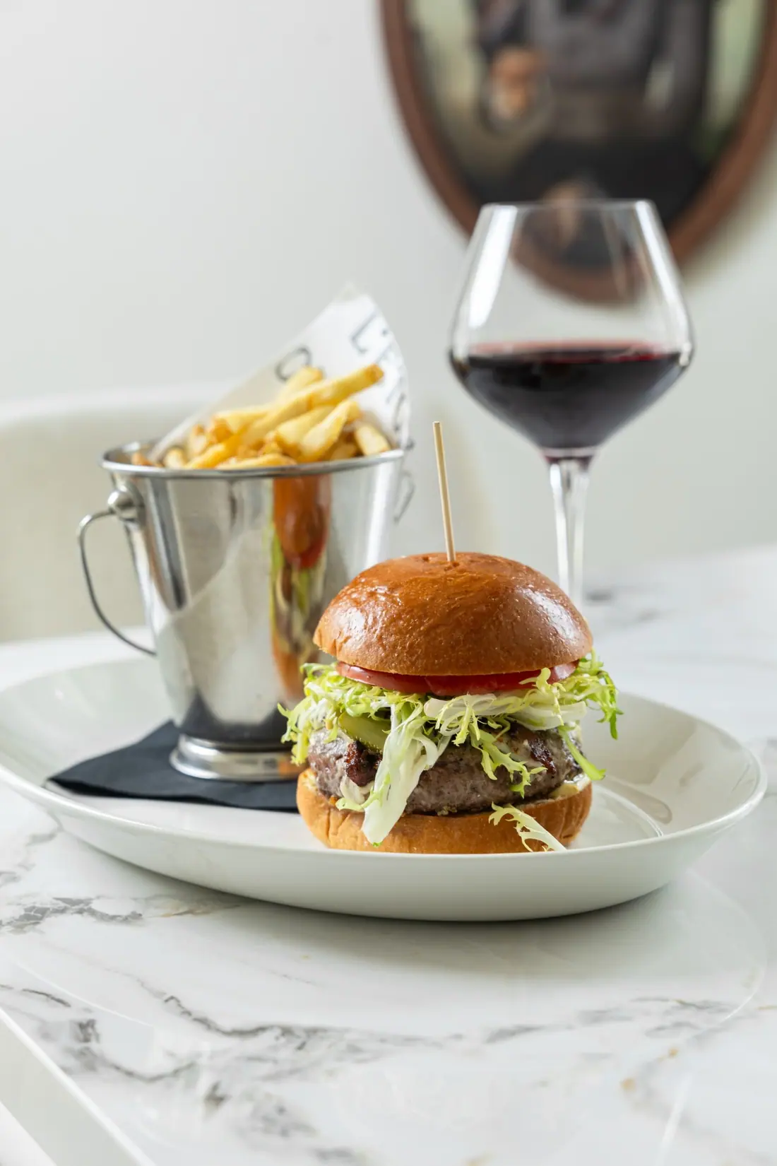 Le Burger L'Étoile with frites and a glass of red wine on a marble table